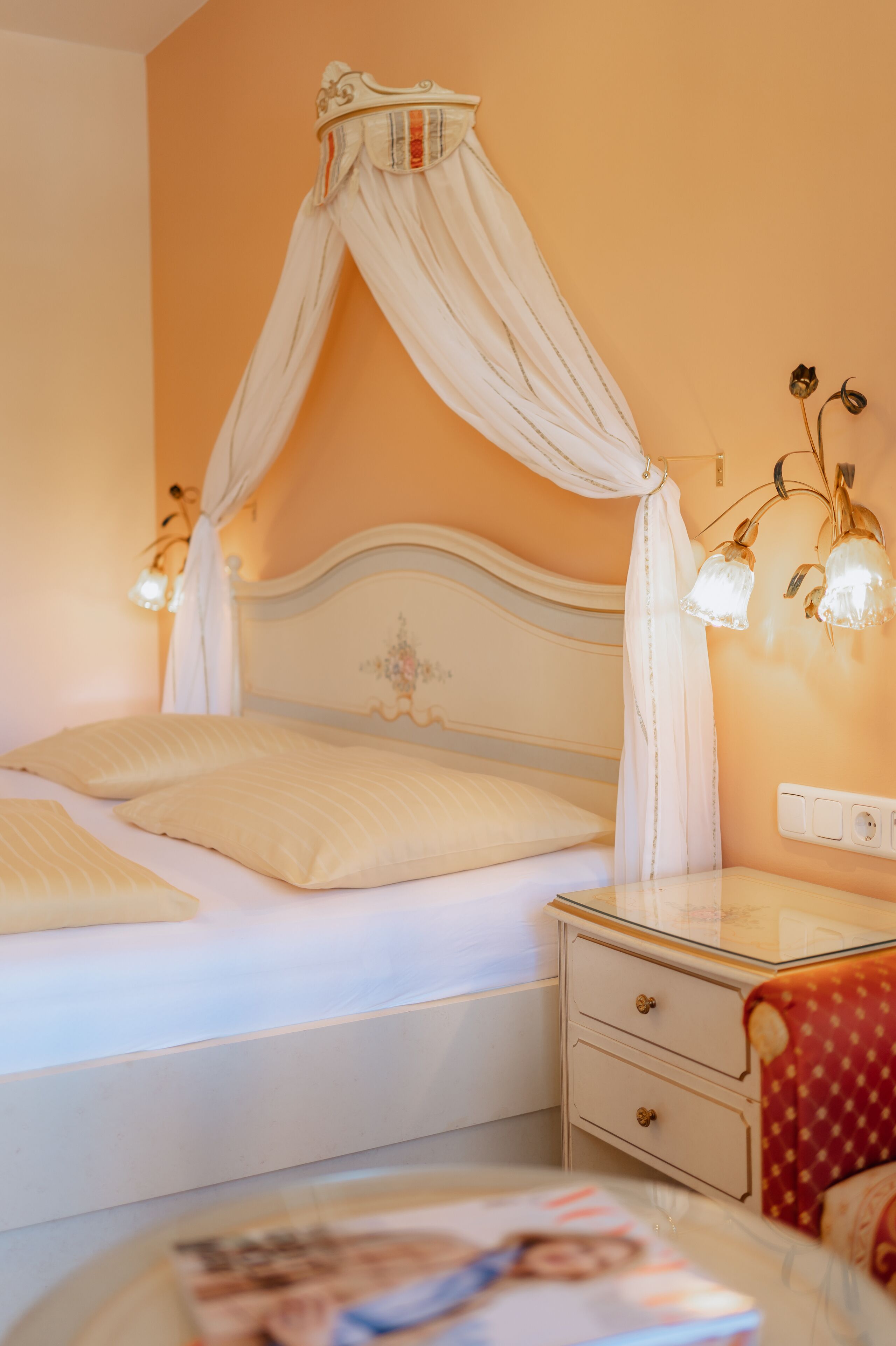Ein Schlafzimmer mit Himmelbett, Nachttisch mit Lampe und einer Kommode.