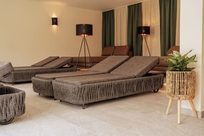 A modern lounge area with multiple reclining sofas, a small round table with a plant, and two floor lamps. - Schlössl Hotel Kindl (Bad Gleichenberg)