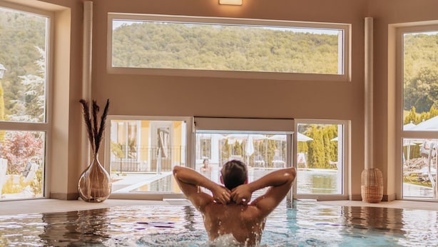 A person in a swimming pool with large windows and wooden beams. - Schlössl Hotel Kindl (Bad Gleichenberg)
