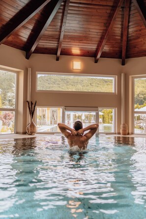 Una persona in piscina, con ampie finestre e travi in legno.