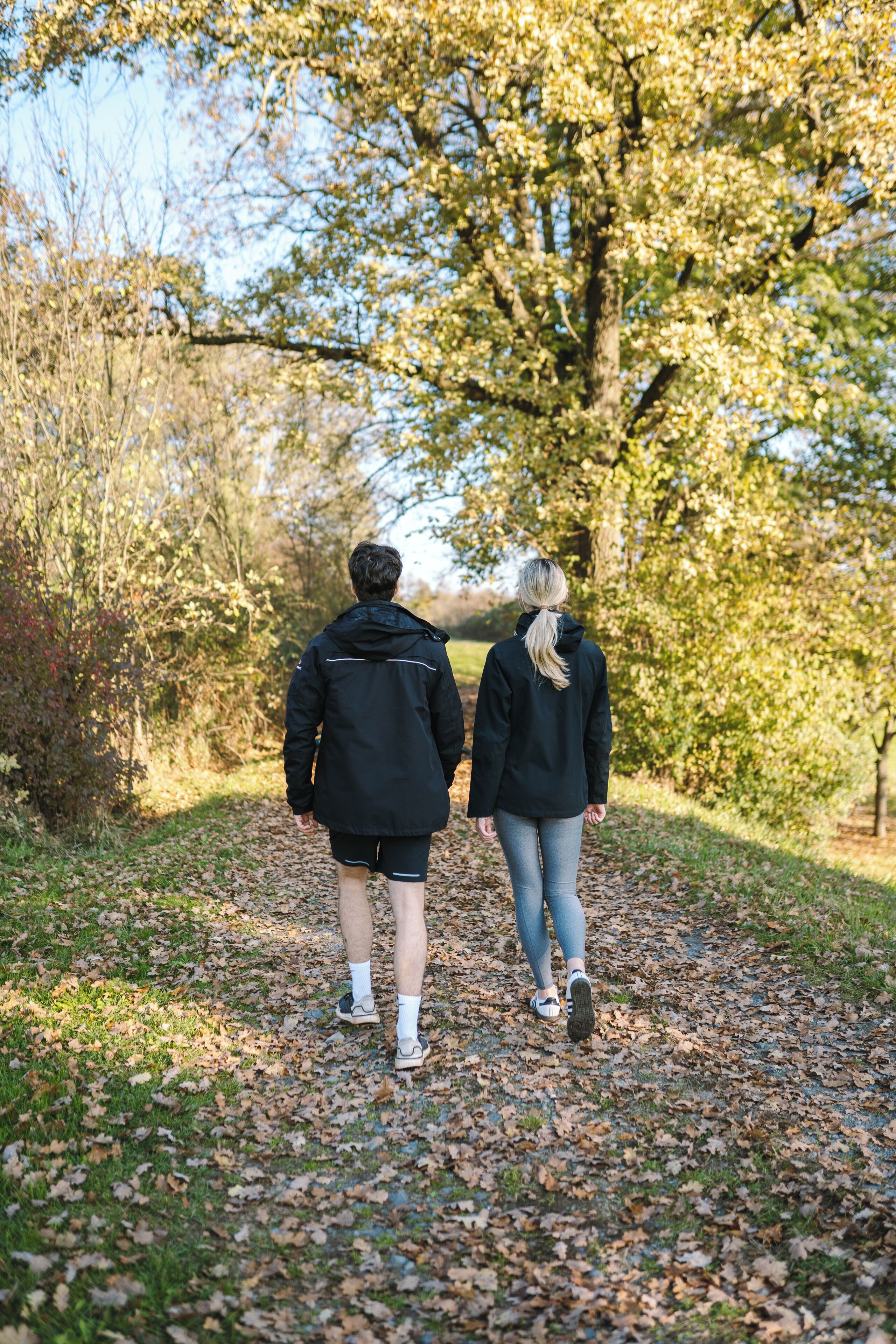 A couple walking on a leaf-covered path in a park.