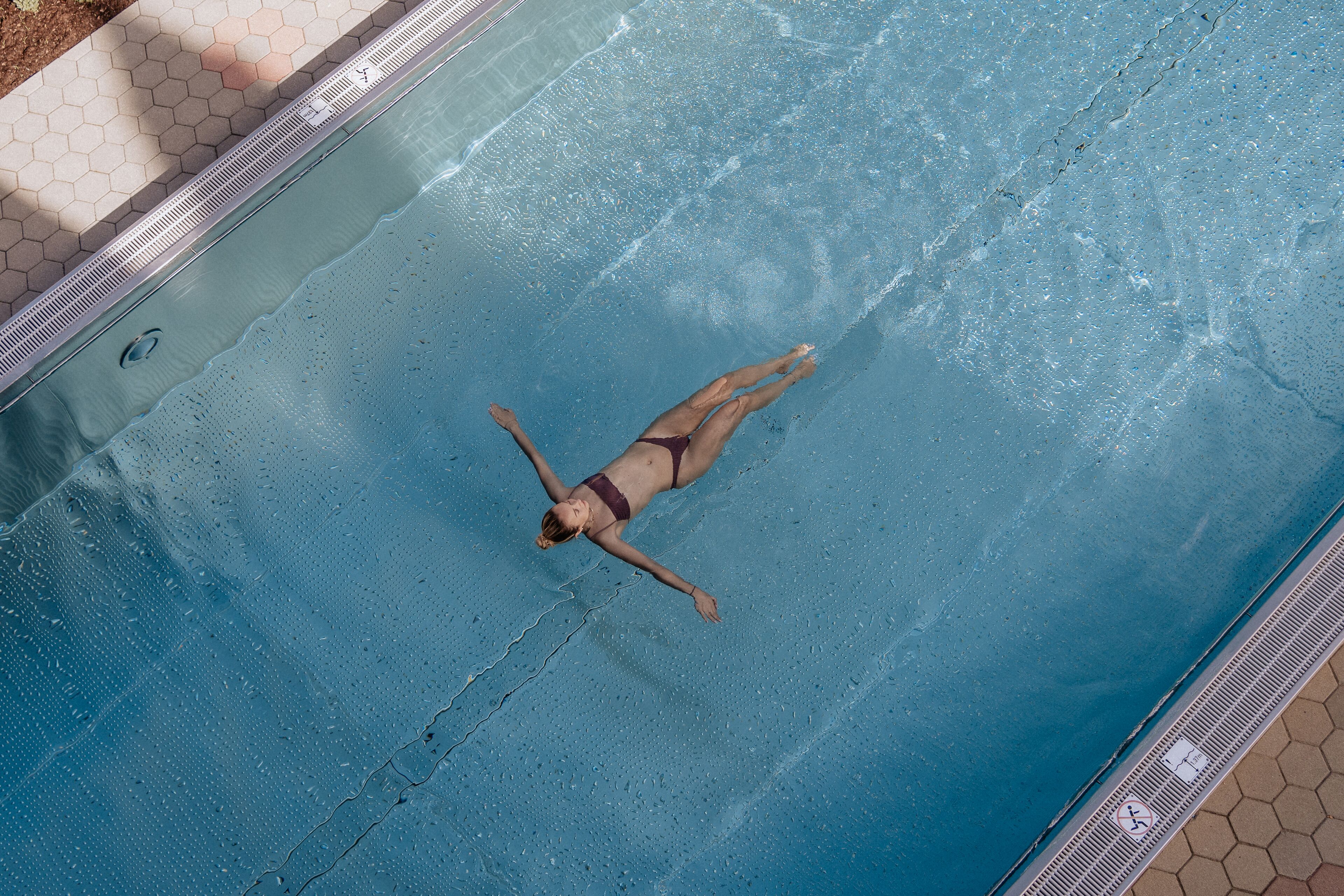 A person floating in a swimming pool with a tiled edge and a hexagonal pattern on the side.