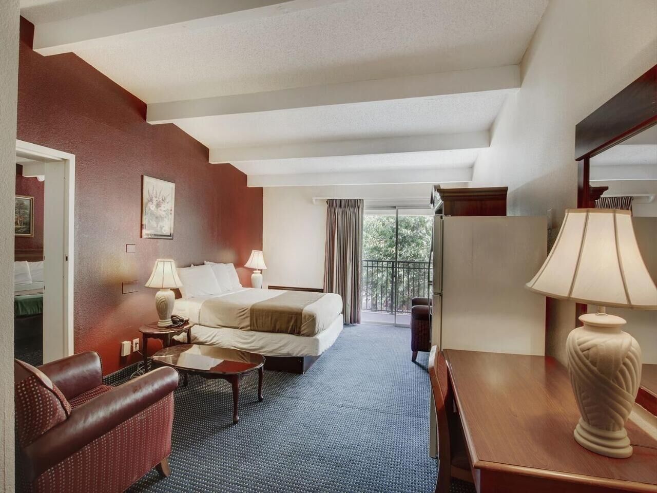Habitación de hotel con cama, escritorio, silla, lámpara y vistas al exterior.