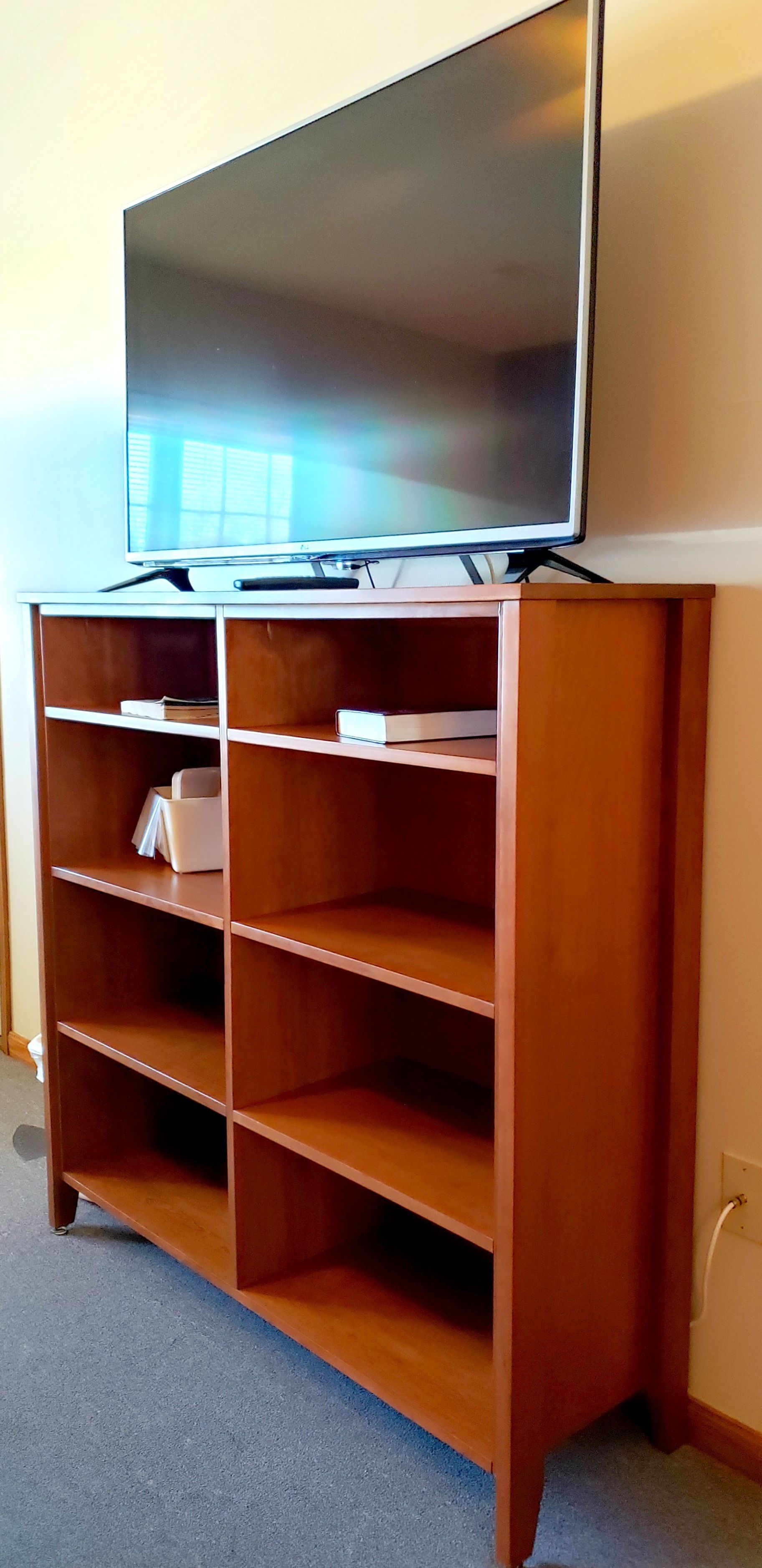 A wooden entertainment center with a flat-screen TV on top, multiple shelves, and a power outlet on the right.
