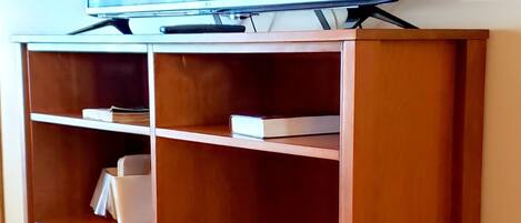 A wooden entertainment center with a flat-screen TV on top, multiple shelves, and a power outlet on the right.