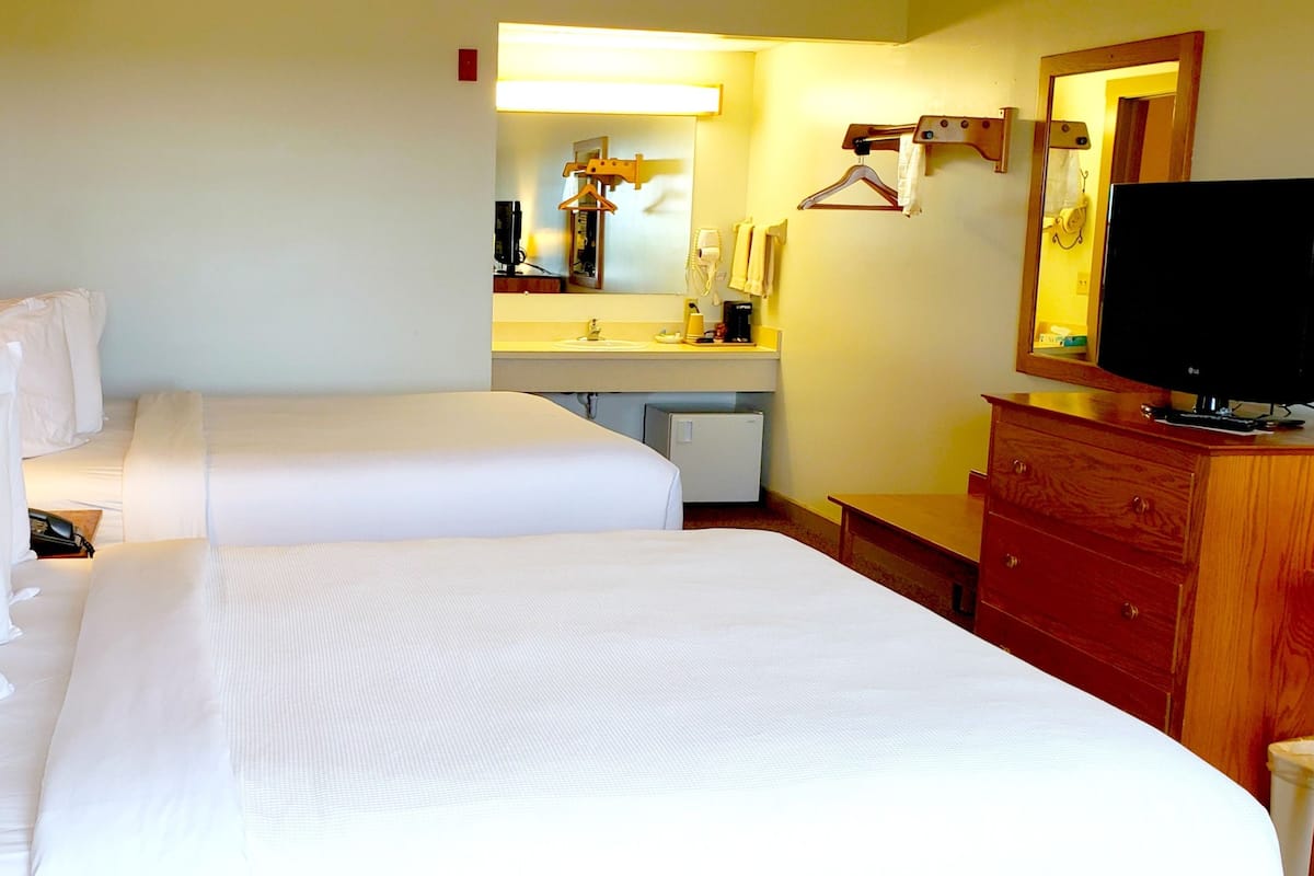 A hotel room with two beds, a wooden dresser, a television, and a bathroom visible through an open door.