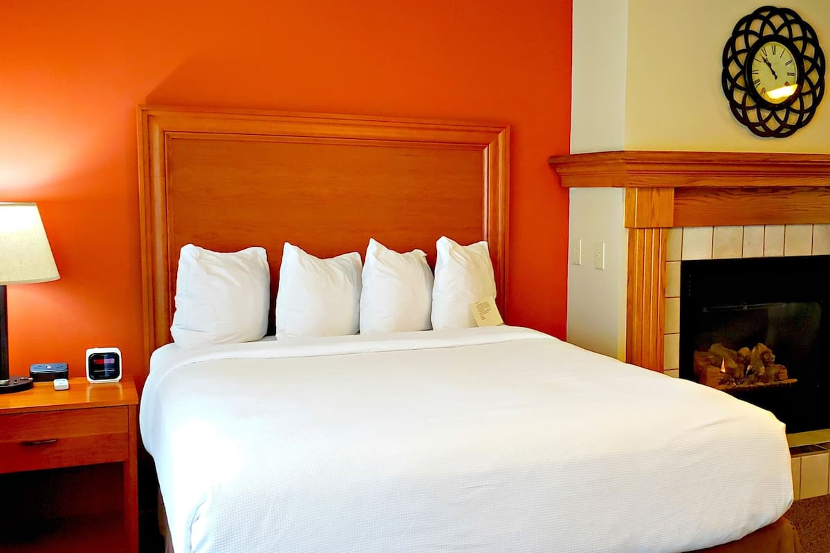 A hotel room with a large bed, a nightstand with a lamp, a fireplace, and a television.