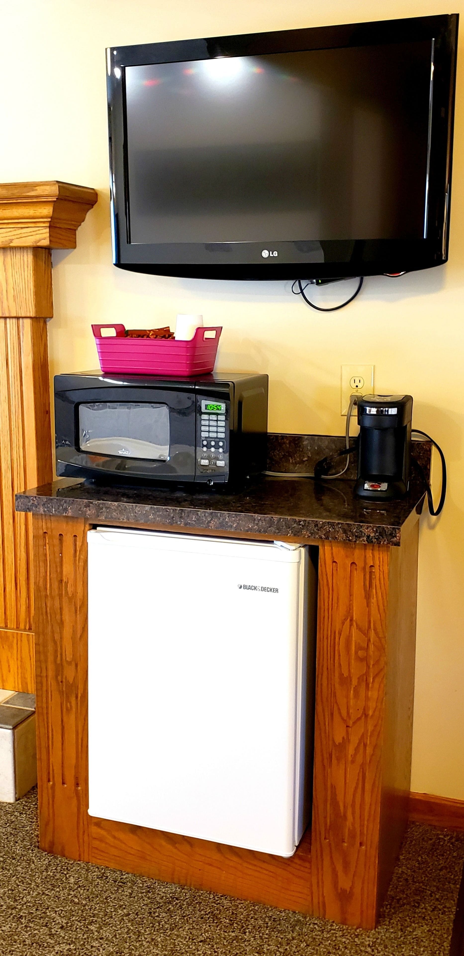 A kitchenette with a microwave, a small refrigerator, a coffee maker, and a flat-screen TV mounted on the wall.