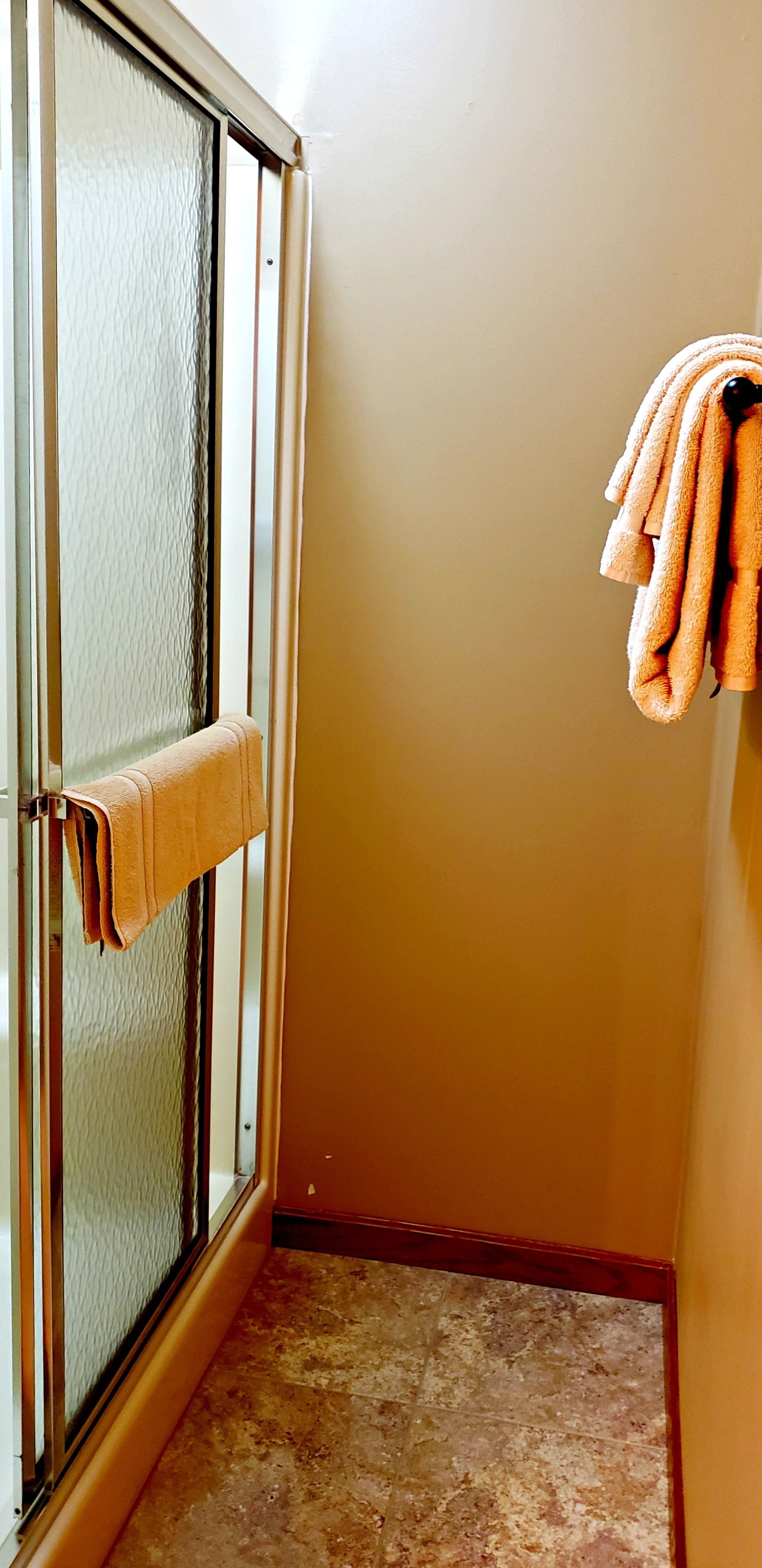 Un baño con puerta de vidrio, un perchero con una toalla y suelo de baldosas.