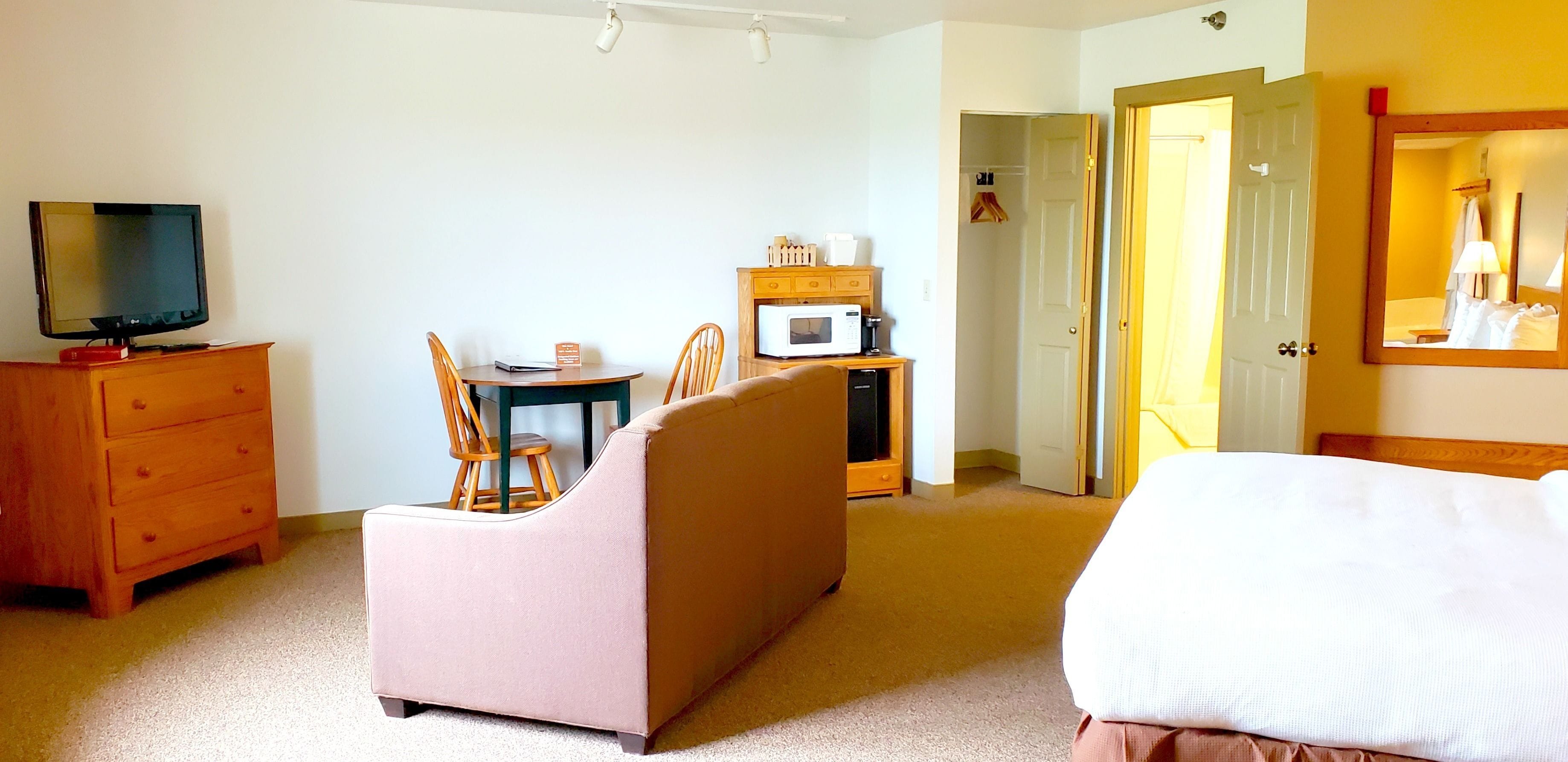 A hotel room with a bed, a TV, a desk with a chair, a microwave, and a wardrobe.