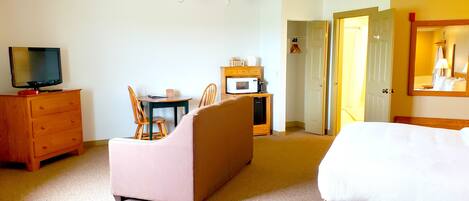 A hotel room with a bed, a TV, a desk with a chair, a microwave, and a wardrobe.