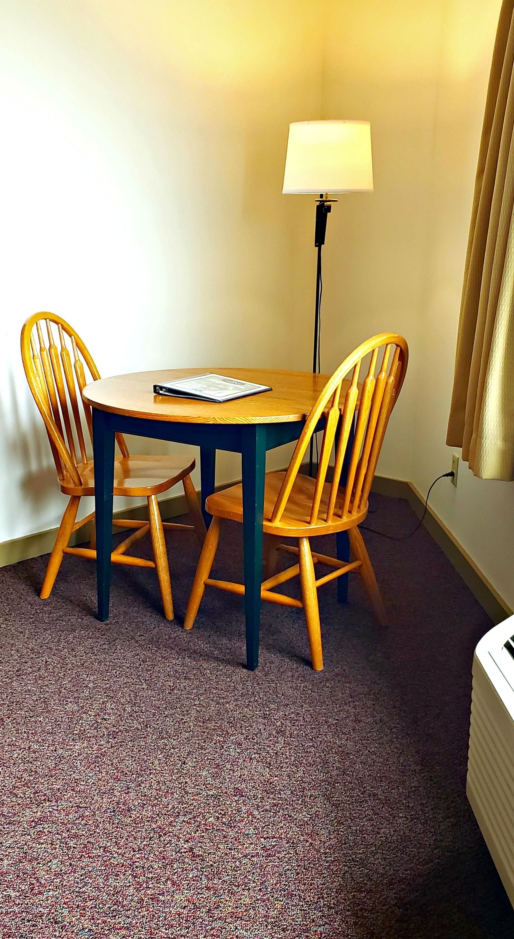 A small round table with four wooden chairs, a lamp, and a carpeted floor.