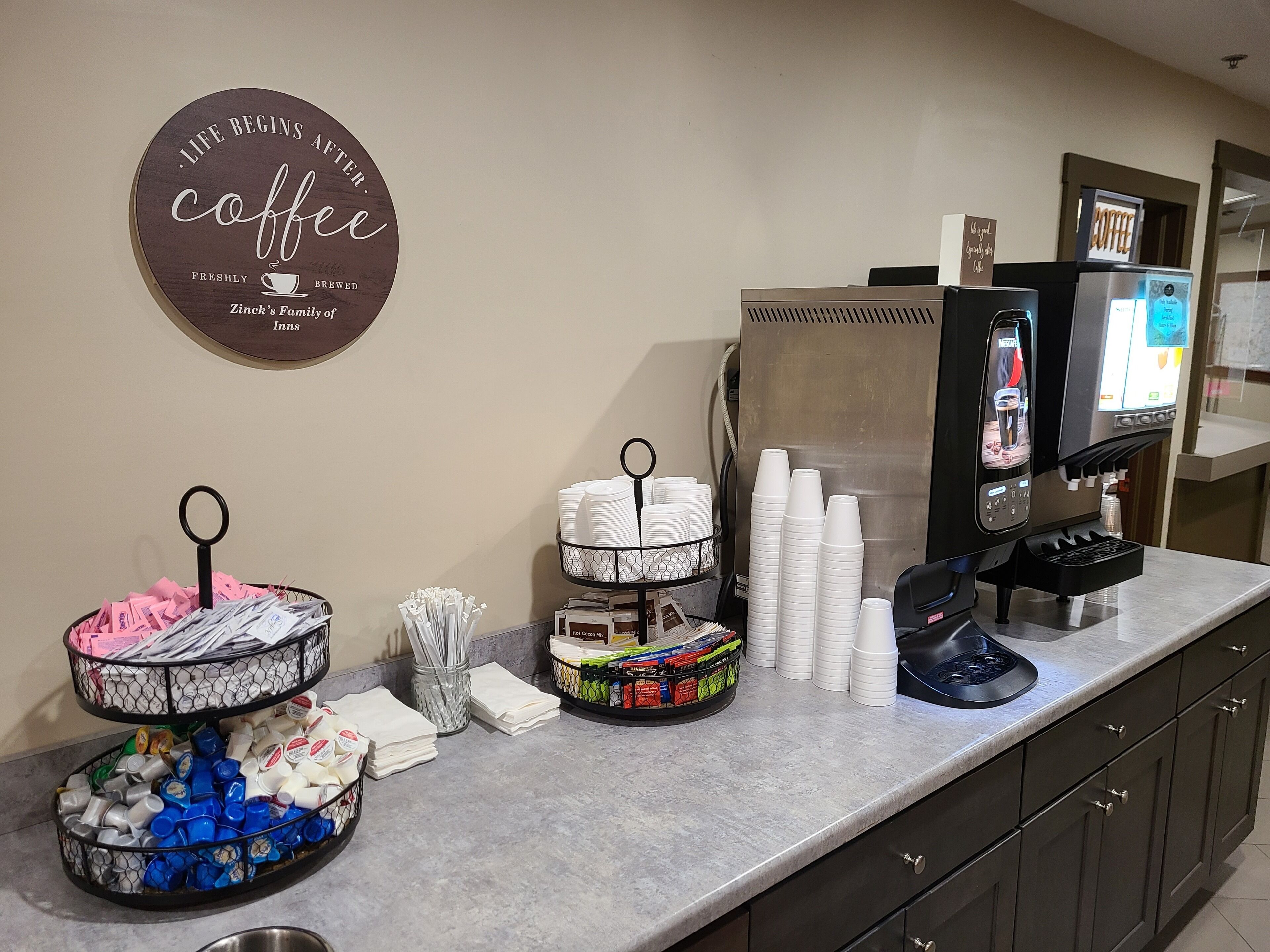 A coffee station with a coffee sign, a coffee machine, and various cups and mugs.