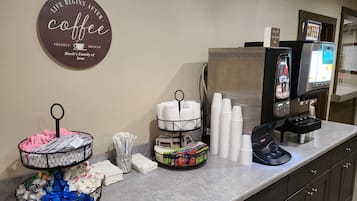A coffee station with a coffee sign, a coffee machine, and various cups and mugs.