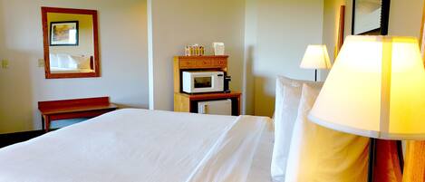 A hotel room with a bed, a bedside table with a lamp, a microwave, and a dresser.