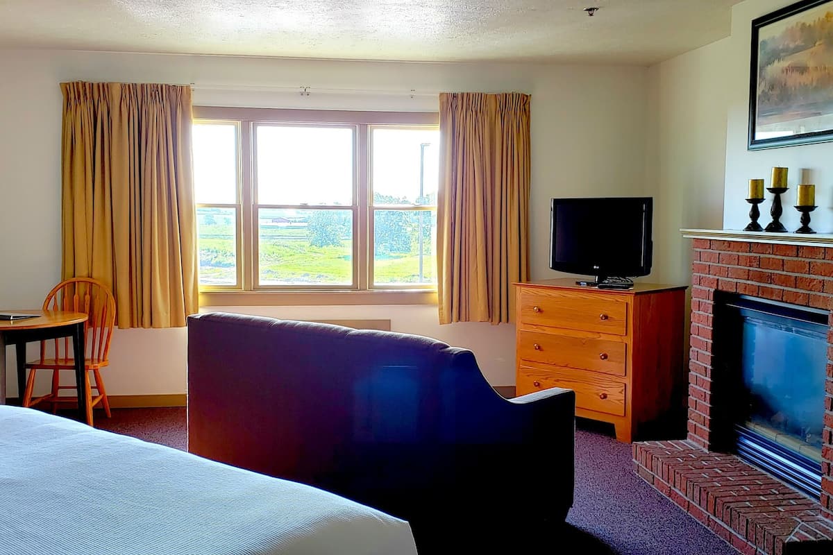 A hotel room with a bed, a TV, a fireplace, a window with curtains, and a view of the outdoors.