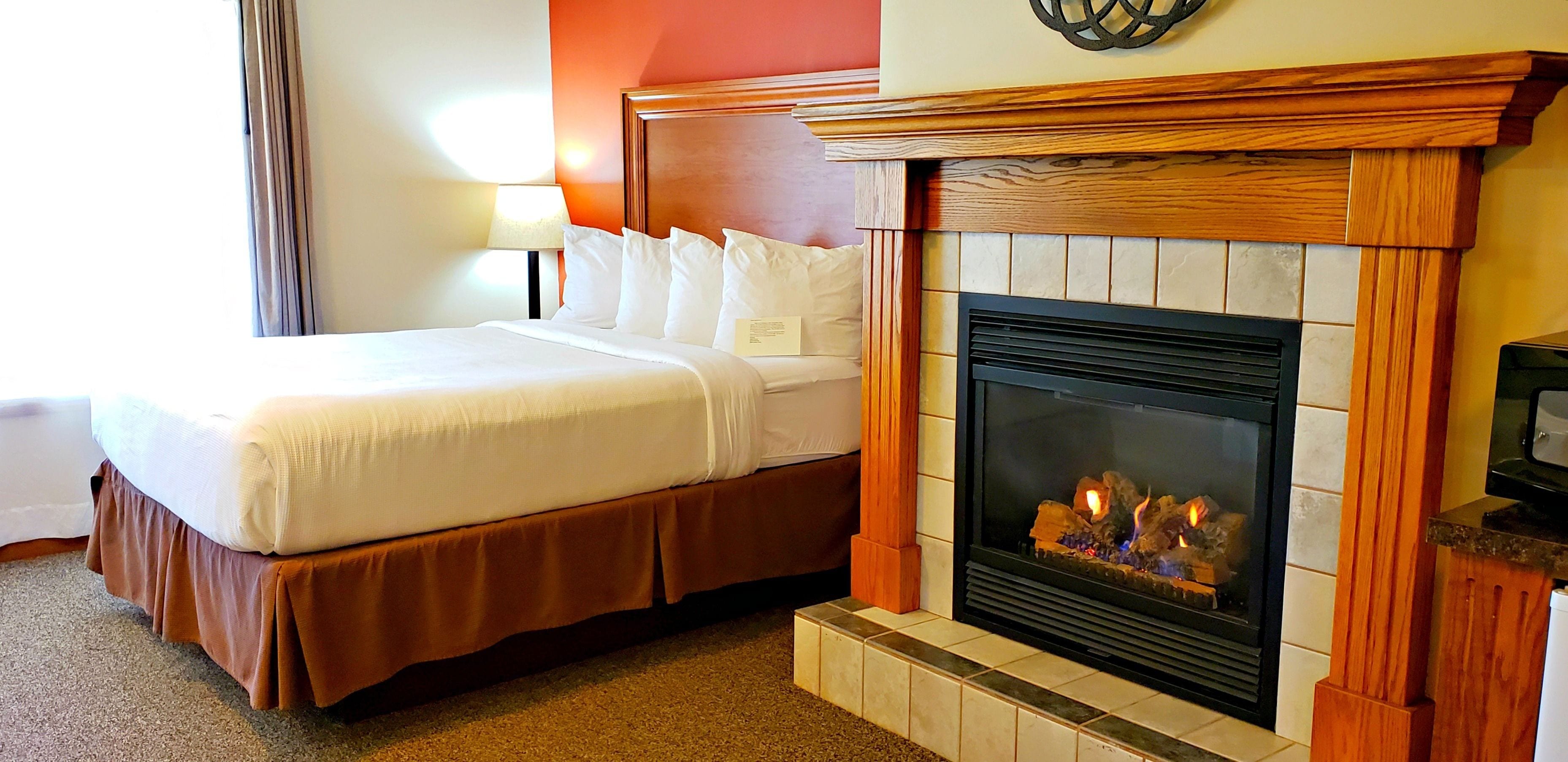 Une chambre d’hôtel avec un grand lit, une cheminée et une table de chevet avec une lampe.
