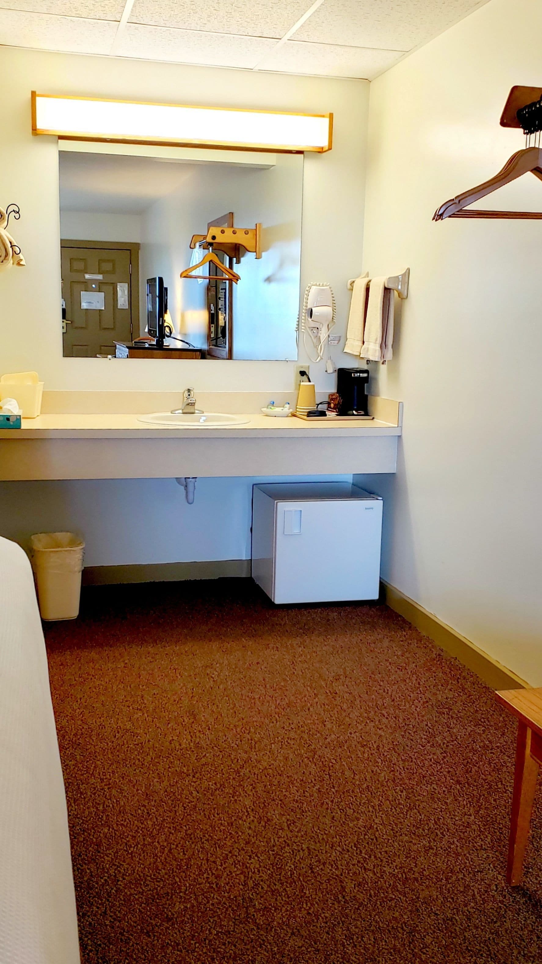 A hotel bathroom with a sink, mirror, towel rack, and a small white cabinet.