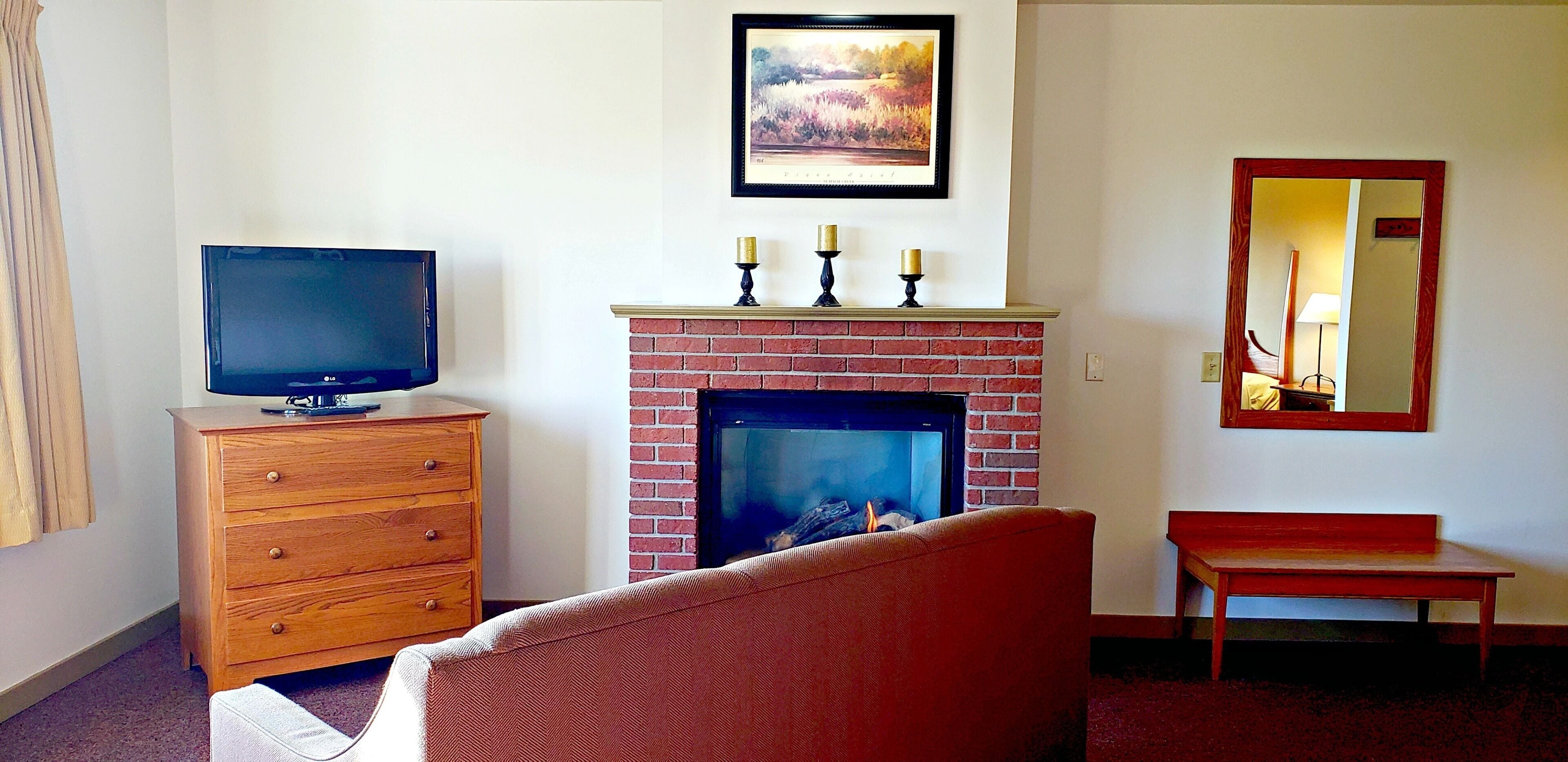 A living room with a television, a fireplace, a bench, and a mirror.