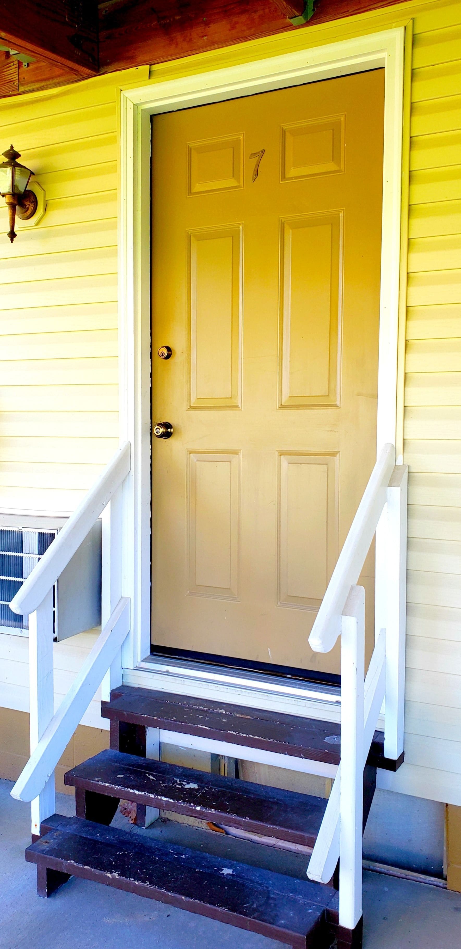 A yellow house with a brown door and white steps leading up to it.