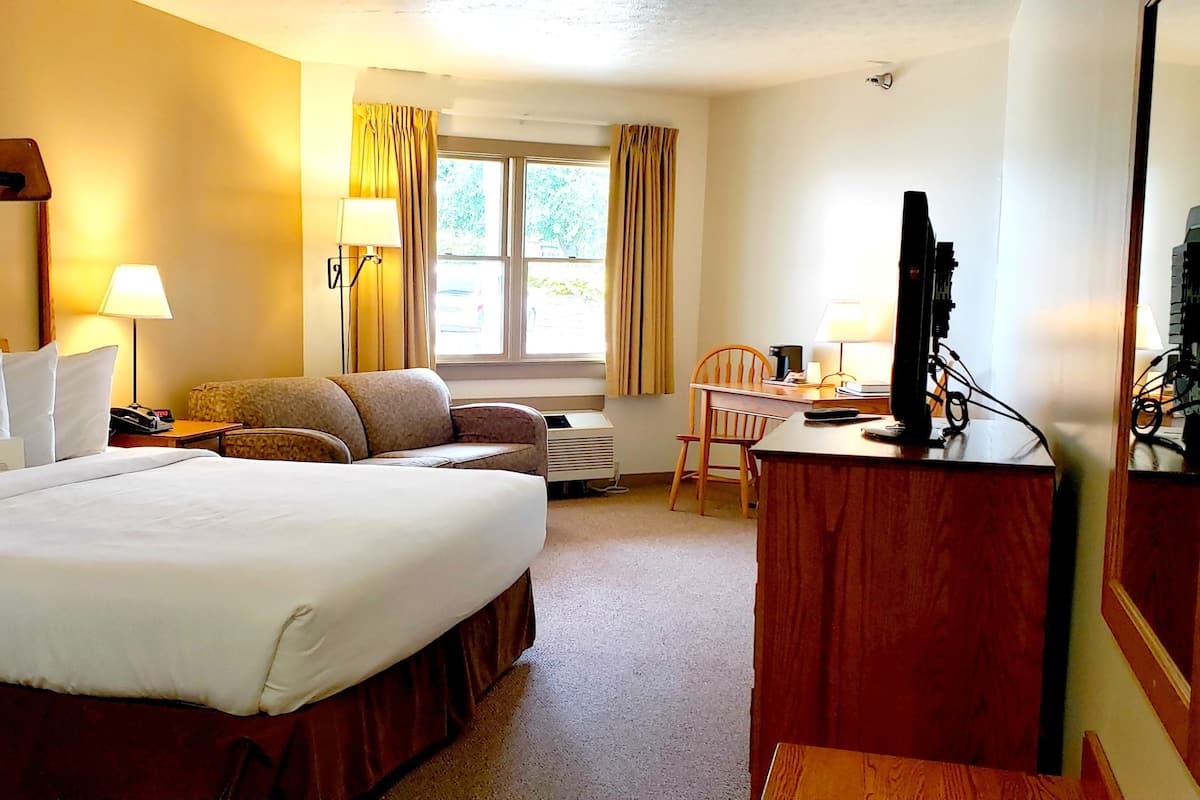A hotel room with a large bed, a desk with a chair, a TV, and a window with curtains.