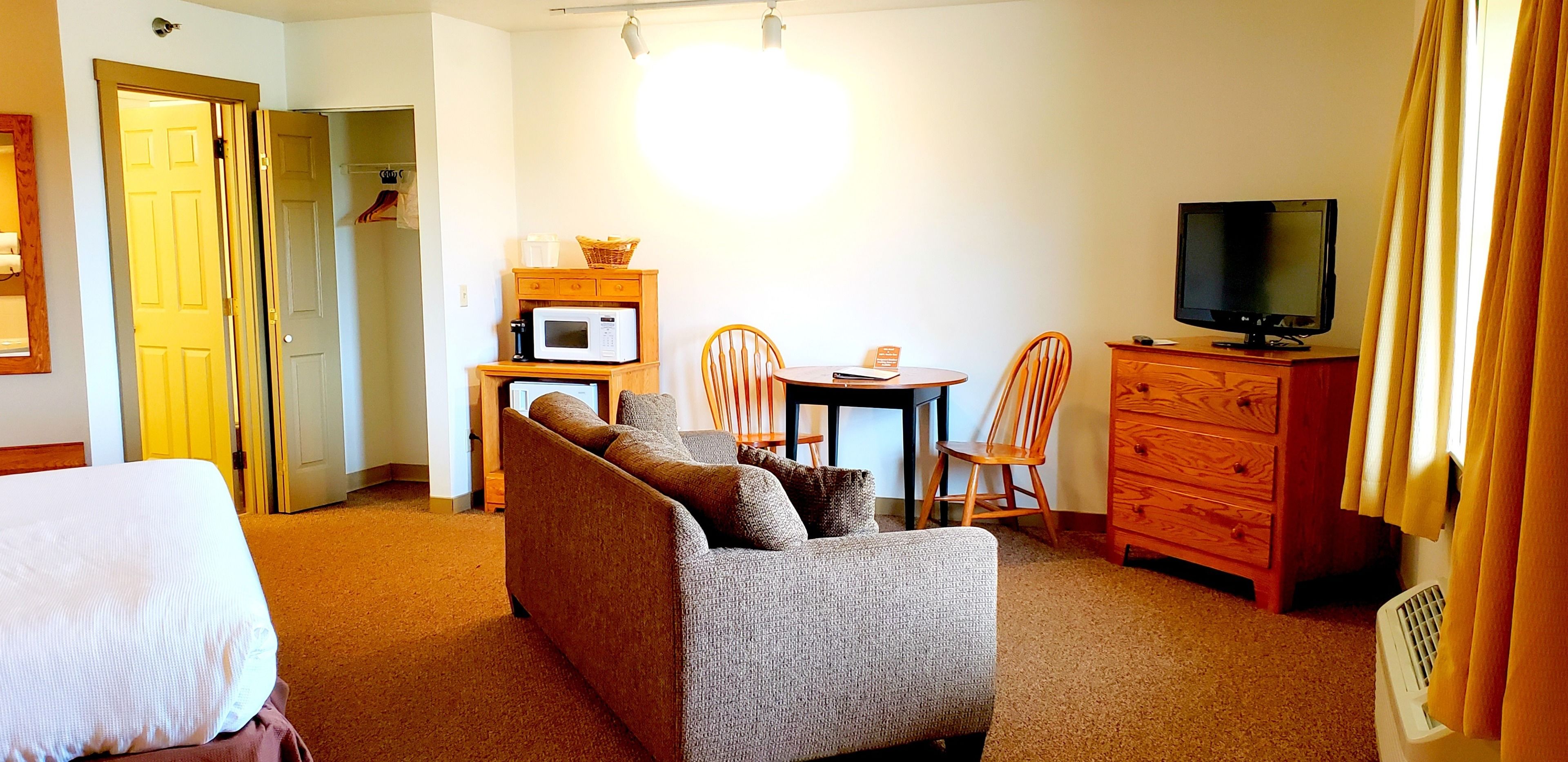 A hotel room with a sofa, a TV, a microwave, a small table, and a dresser.