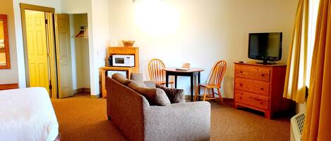 A hotel room with a sofa, a TV, a microwave, a small table, and a dresser.