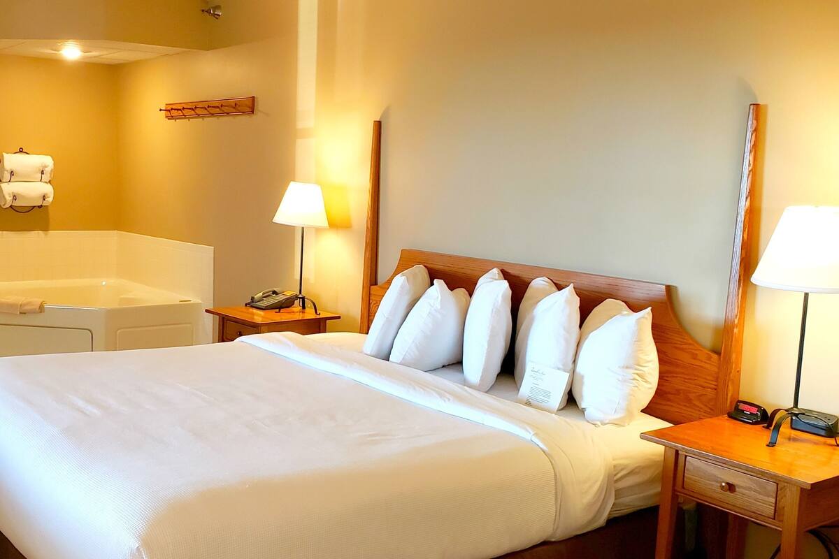 A hotel room with a large bed, bedside lamps, a wooden nightstand, a small table, a telephone, and a towel rack.