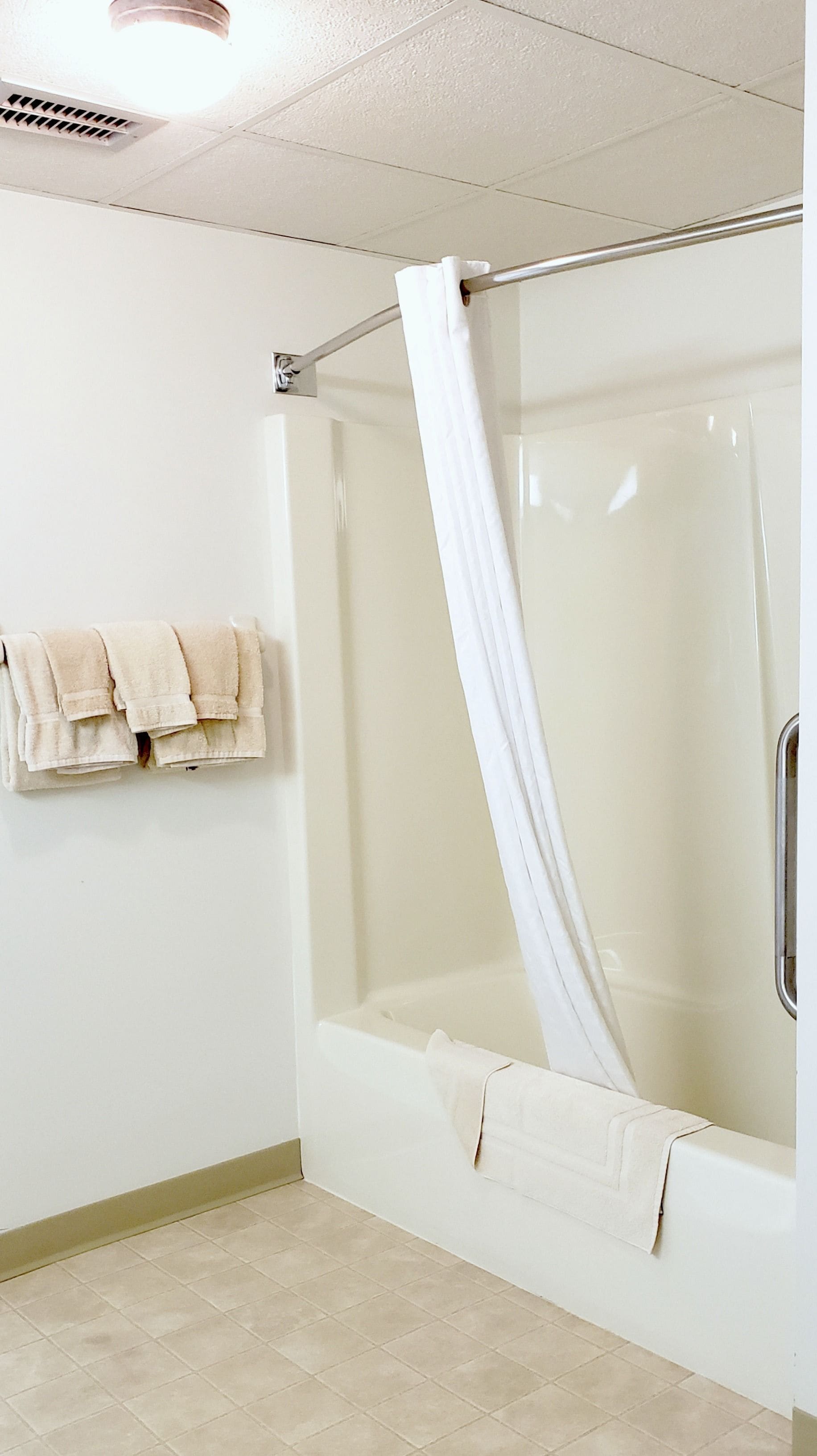 A bathroom with a glass-enclosed shower, a towel rack with folded towels, and a light-colored floor.