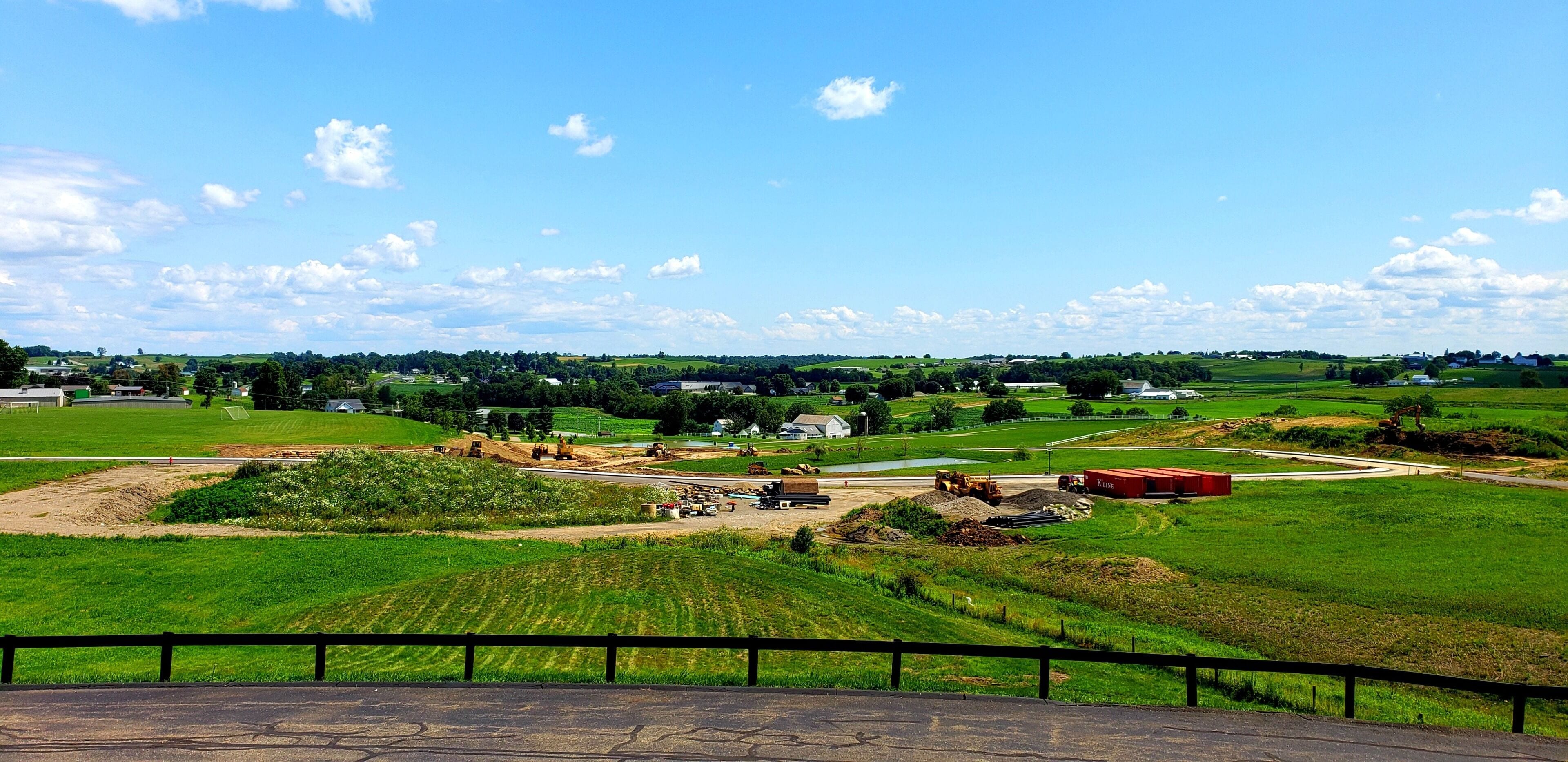 A rural landscape with a road, fields, and a few buildings in the distance.