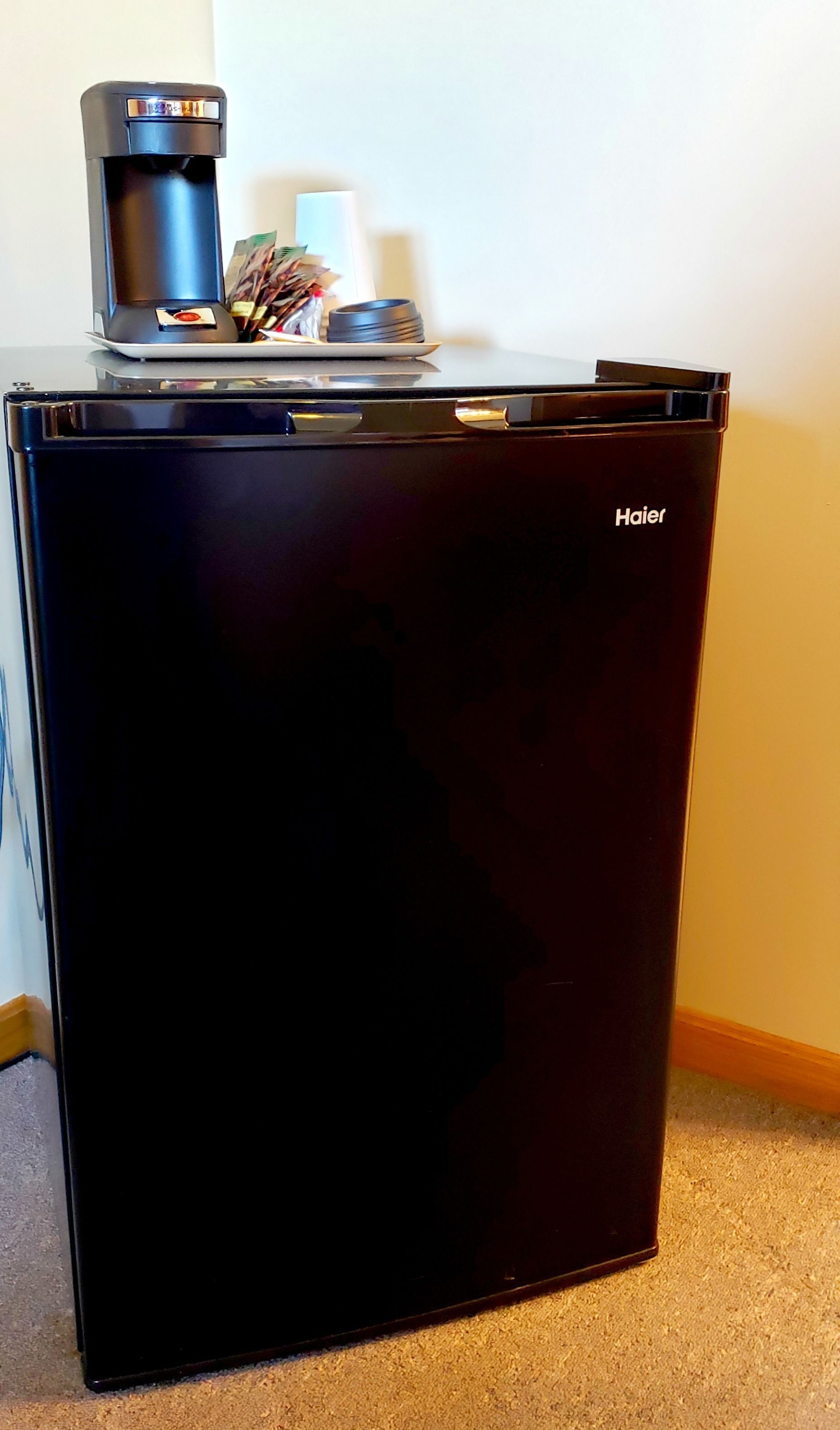 Un refrigerador Haier negro con una cafetera encima.