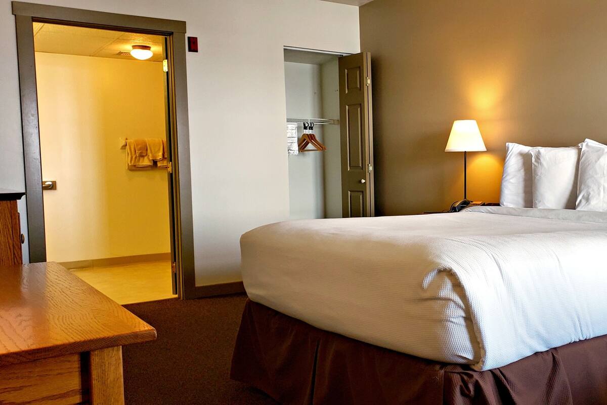 A hotel room with a large bed, a bedside table, a lamp, and a wardrobe.