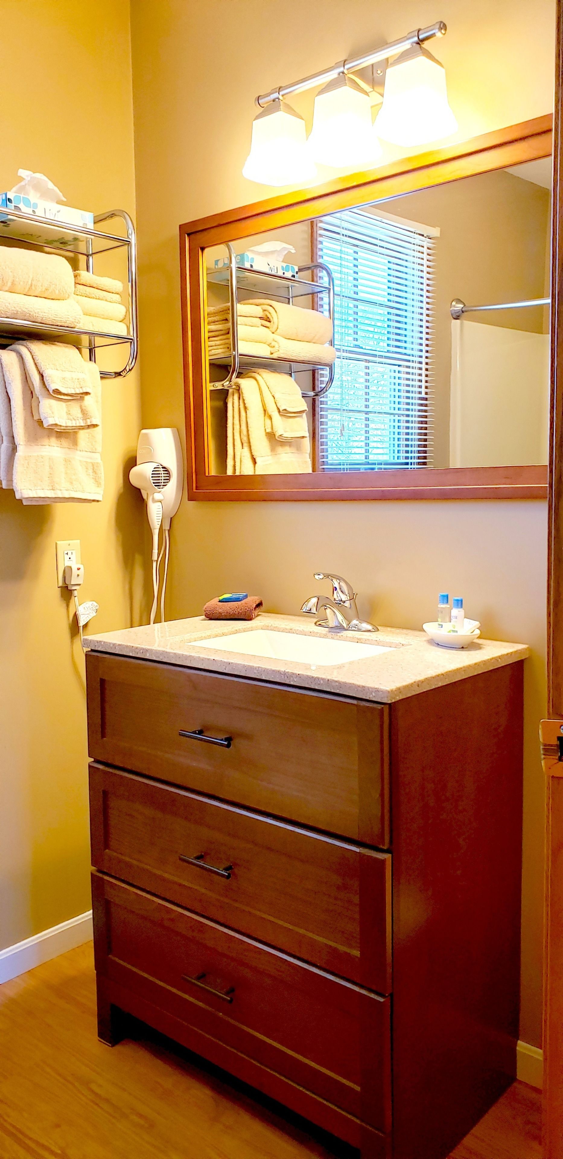 A bathroom with a wooden vanity, a mirror, a towel rack, a hairdryer, and a sink.