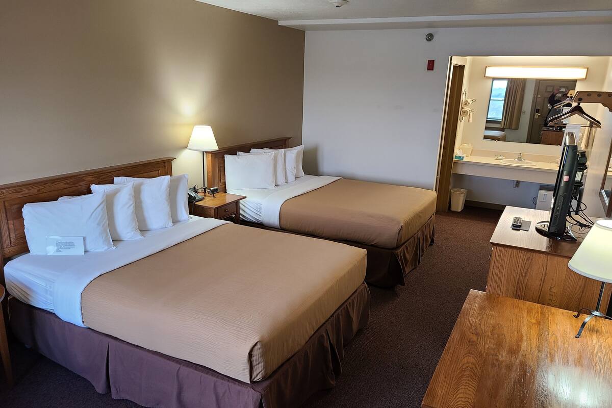 A hotel room with two beds, a desk, a mirror, and a lamp.