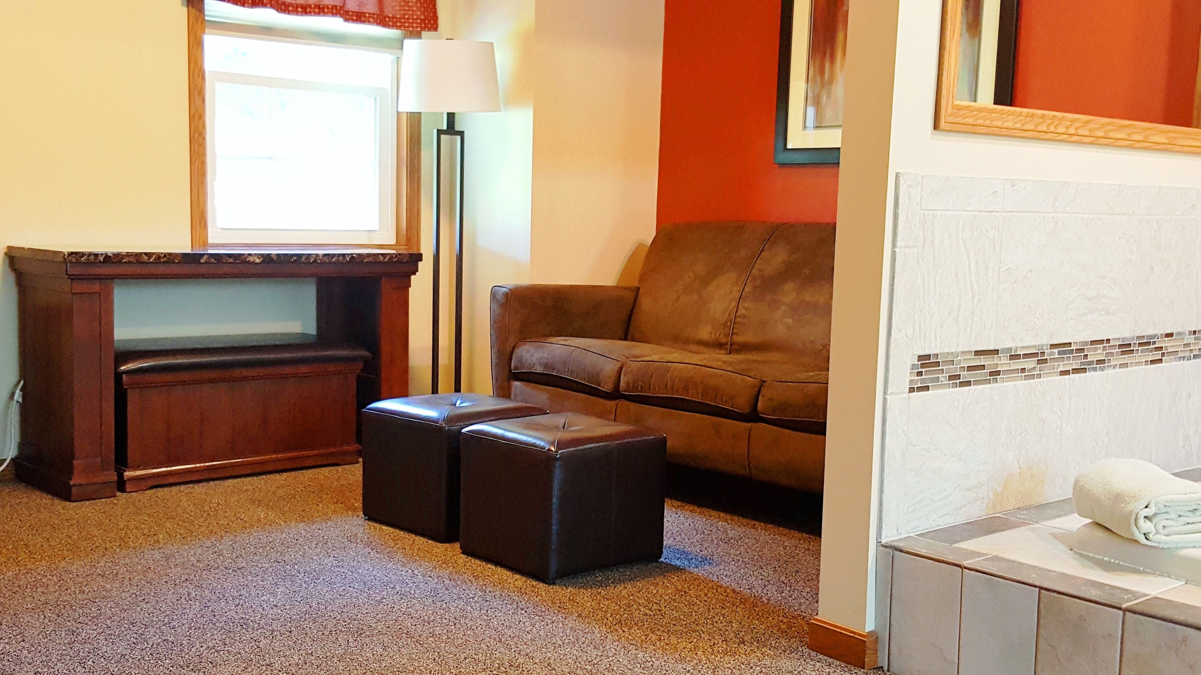 A room with a brown leather sofa, a wooden entertainment unit, and a pair of black ottomans.