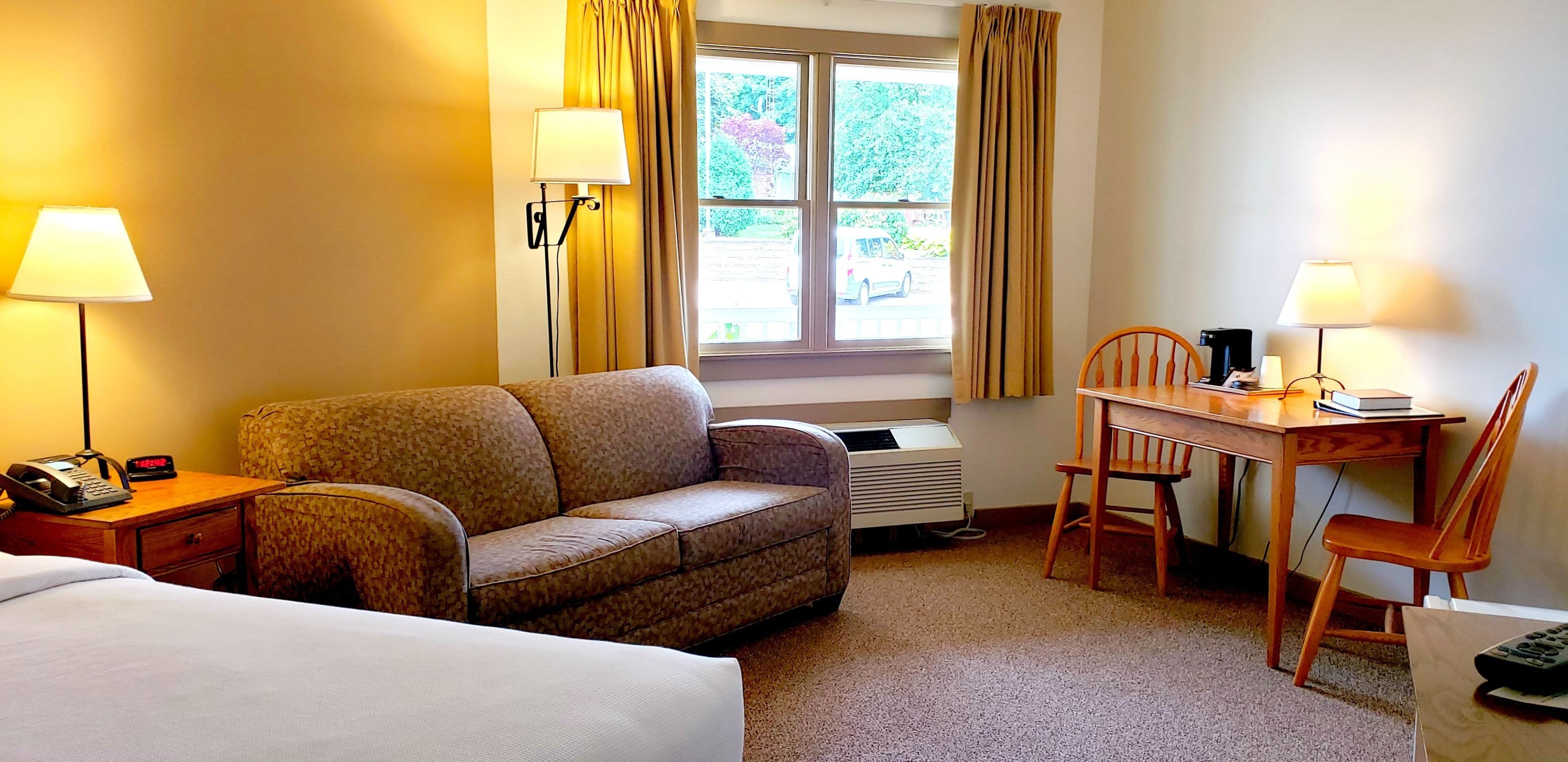 Ein Hotelzimmer mit einem Bett, einer Couch, einem Schreibtisch mit Stuhl, einem Telefon und einem Fenster mit Vorhängen.