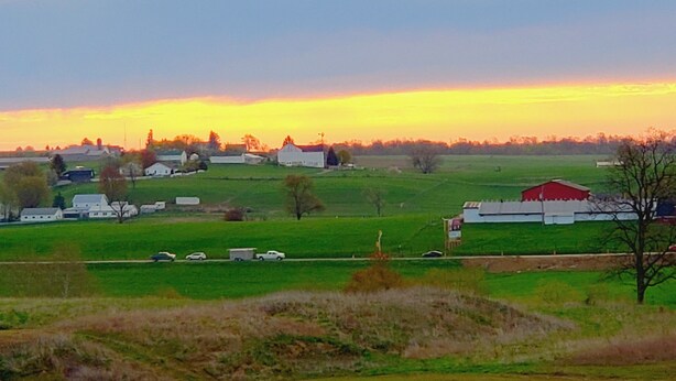 Paisaje rural con un granero, campos abiertos y algunas construcciones dispersas.