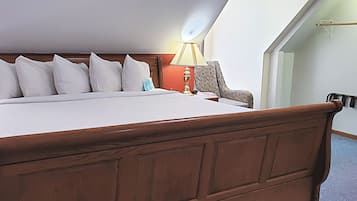 A neatly made bed with a wooden headboard, a bedside lamp, and a chair in a room with a sloped ceiling and a visible door.
