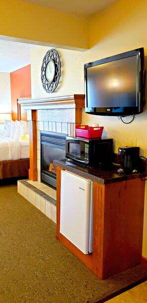A hotel room with a bed, a fireplace, a television, a microwave, and a refrigerator.