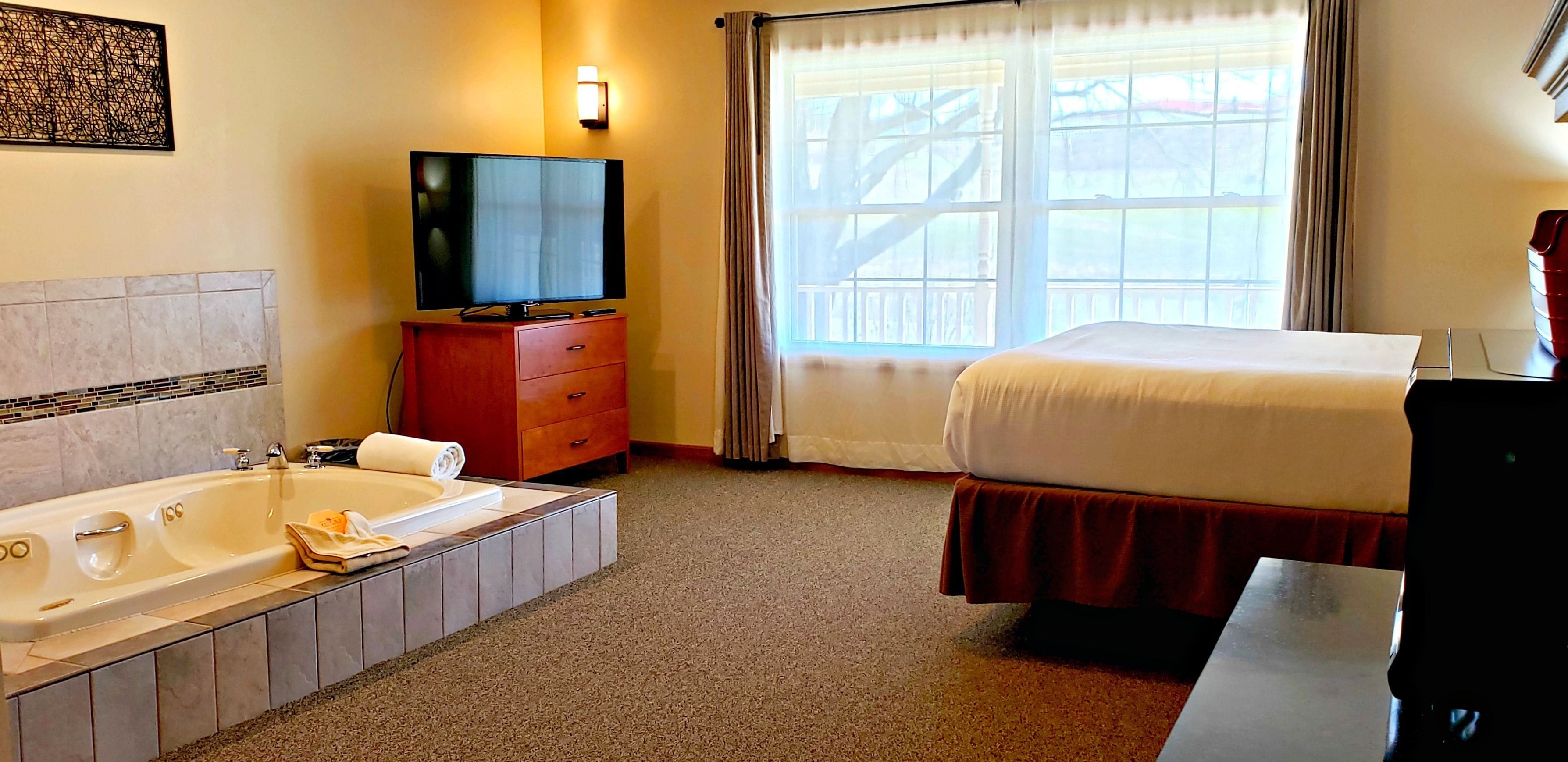 A hotel room with a large bed, a TV on a wooden cabinet, a bathtub, and a window with curtains.