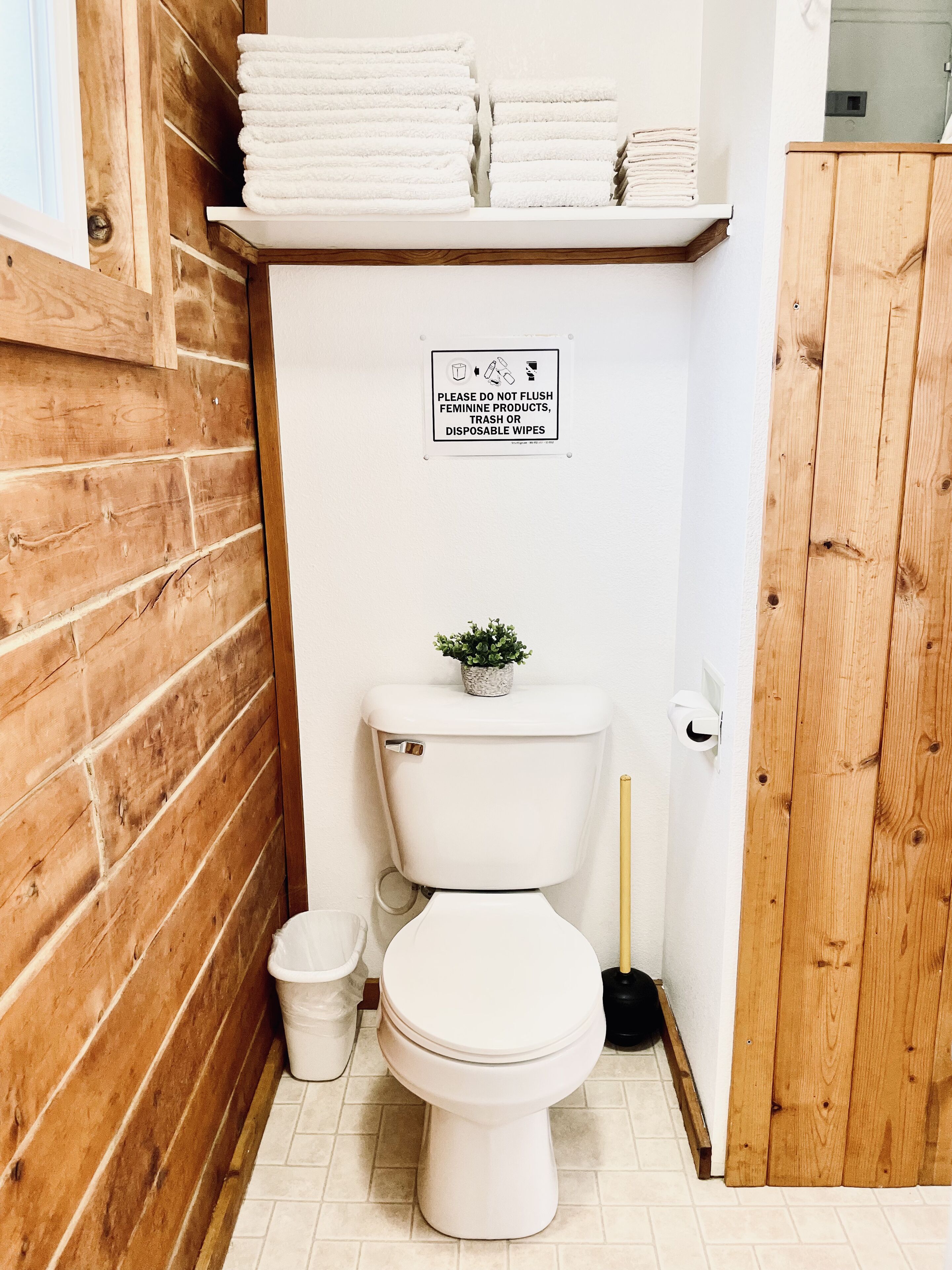 Un baño pequeño y limpio con inodoro, un cubo de basura pequeño y un cartel que prohíbe tirar productos femeninos.