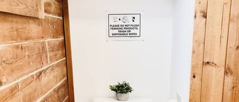 Un baño pequeño y limpio con inodoro, un cubo de basura pequeño y un cartel que prohíbe tirar productos femeninos.
