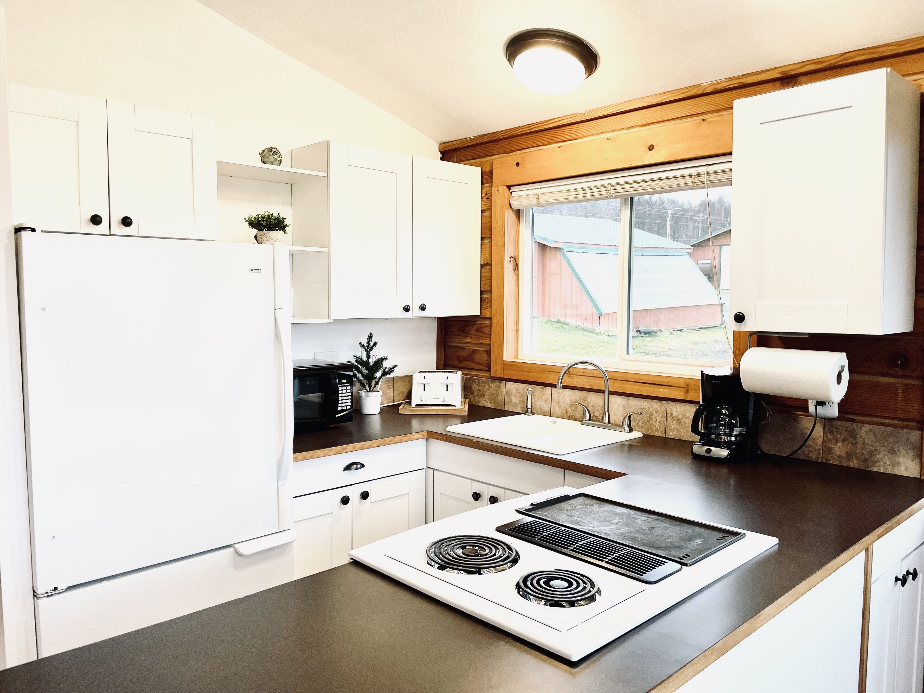 Een moderne keuken met witte kasten, een ingebouwde magnetron, een fornuis en een raam met uitzicht op het buiten.