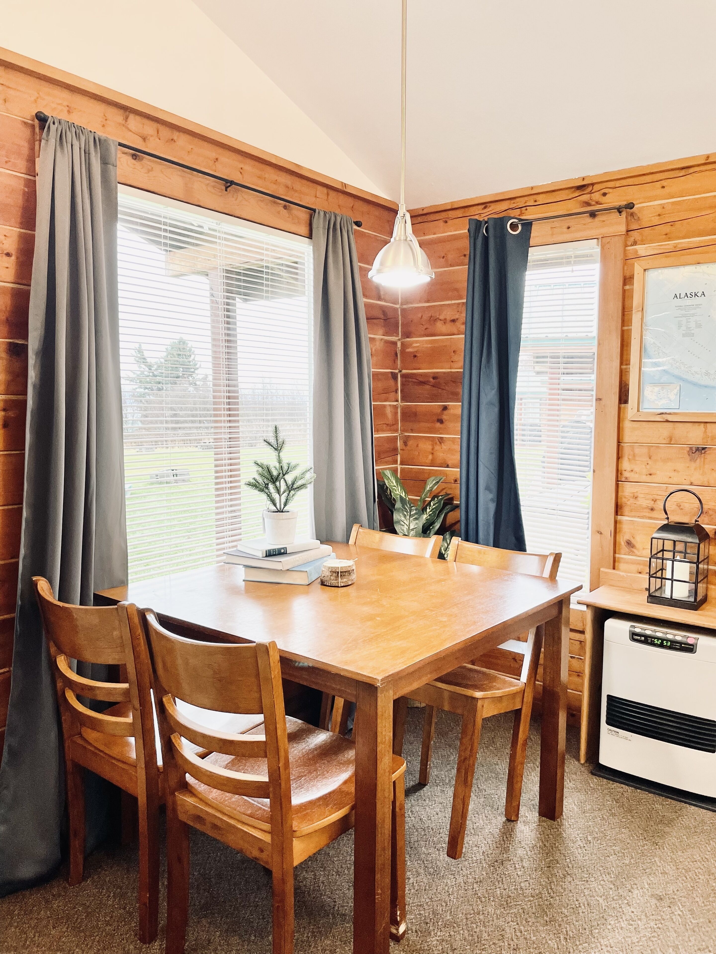A wooden interior with a dining table, chairs, a small potted plant, and a wall-mounted heater.