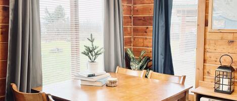 A wooden interior with a dining table, chairs, a small potted plant, and a wall-mounted heater.