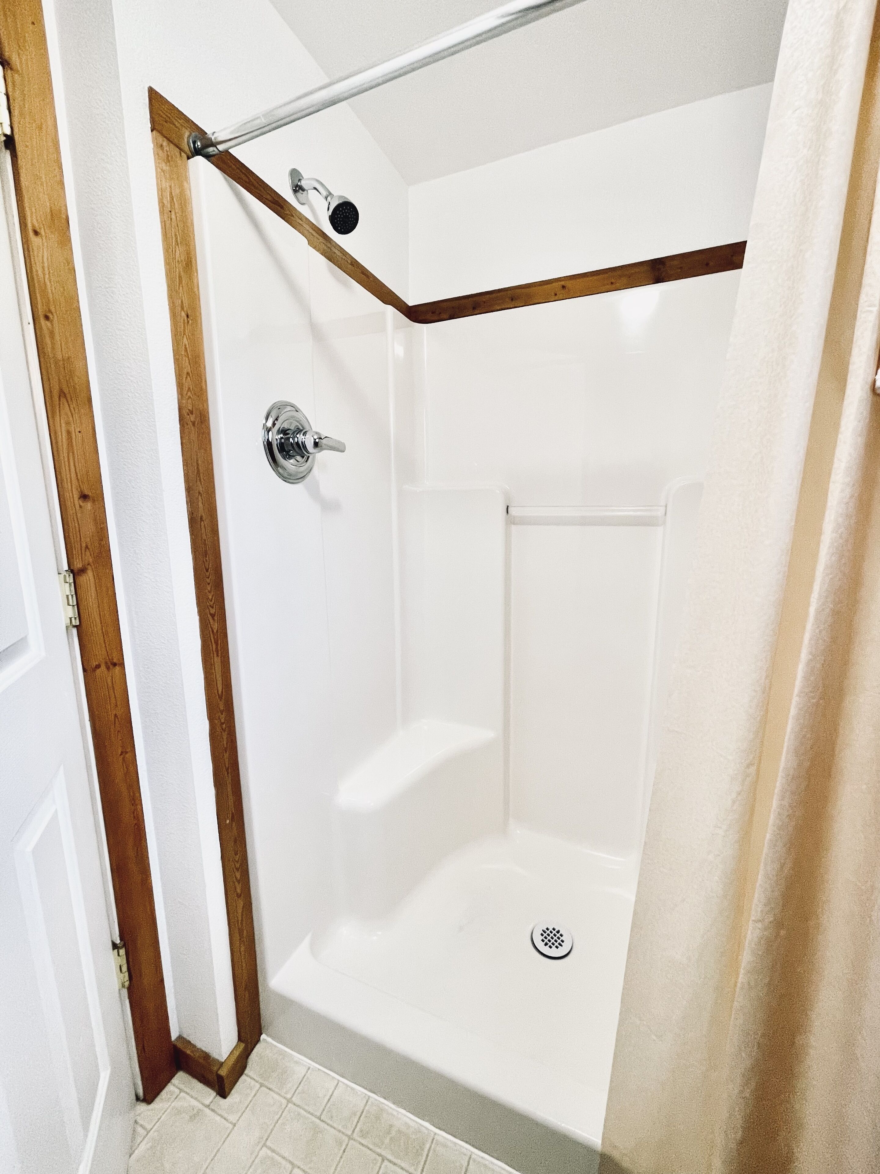 A corner shower with a wooden frame, a chrome faucet, and a drain.