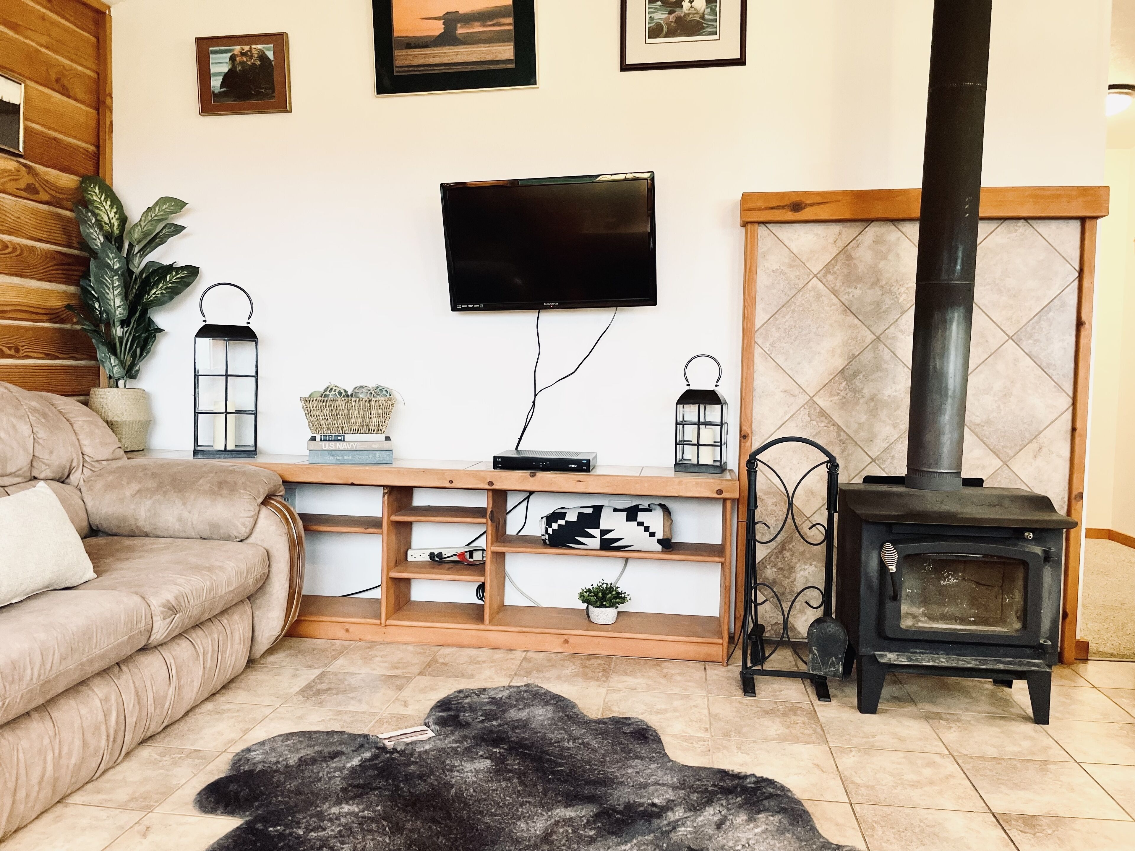 A cozy living room with a sofa, a TV mounted on the wall, a wooden console table with decorative items, and a wood-burning stove.