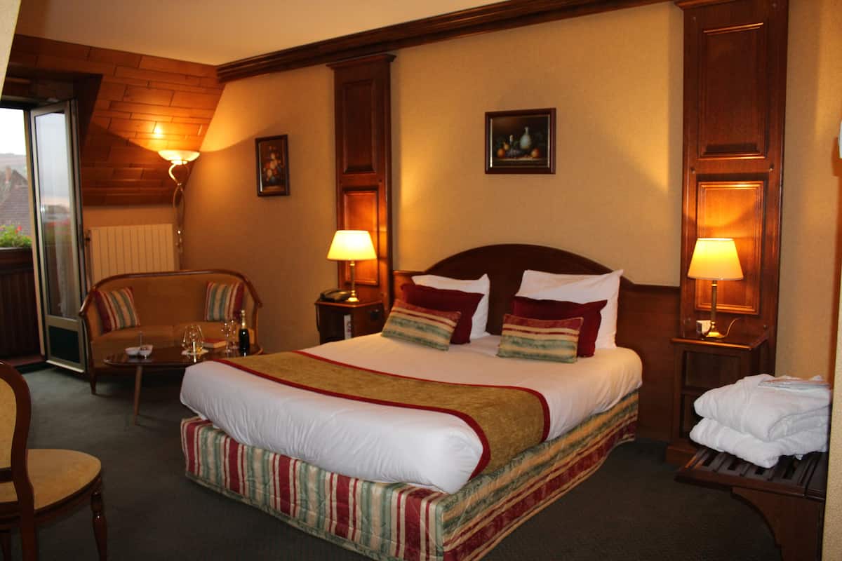 Una habitación de hotel con una cama grande, dos mesitas de noche con lámparas, un sofá y una silla.