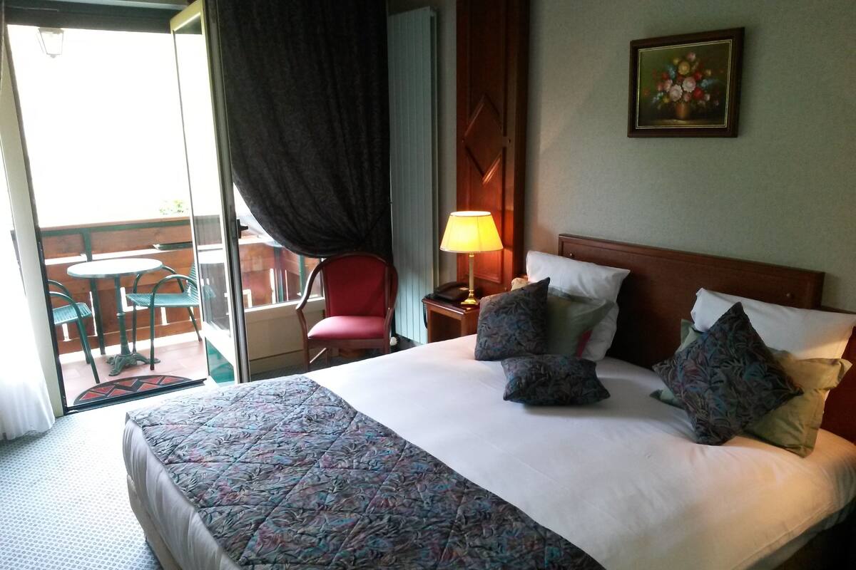 Habitación de hotel con cama, una silla, una mesa y un balcón.