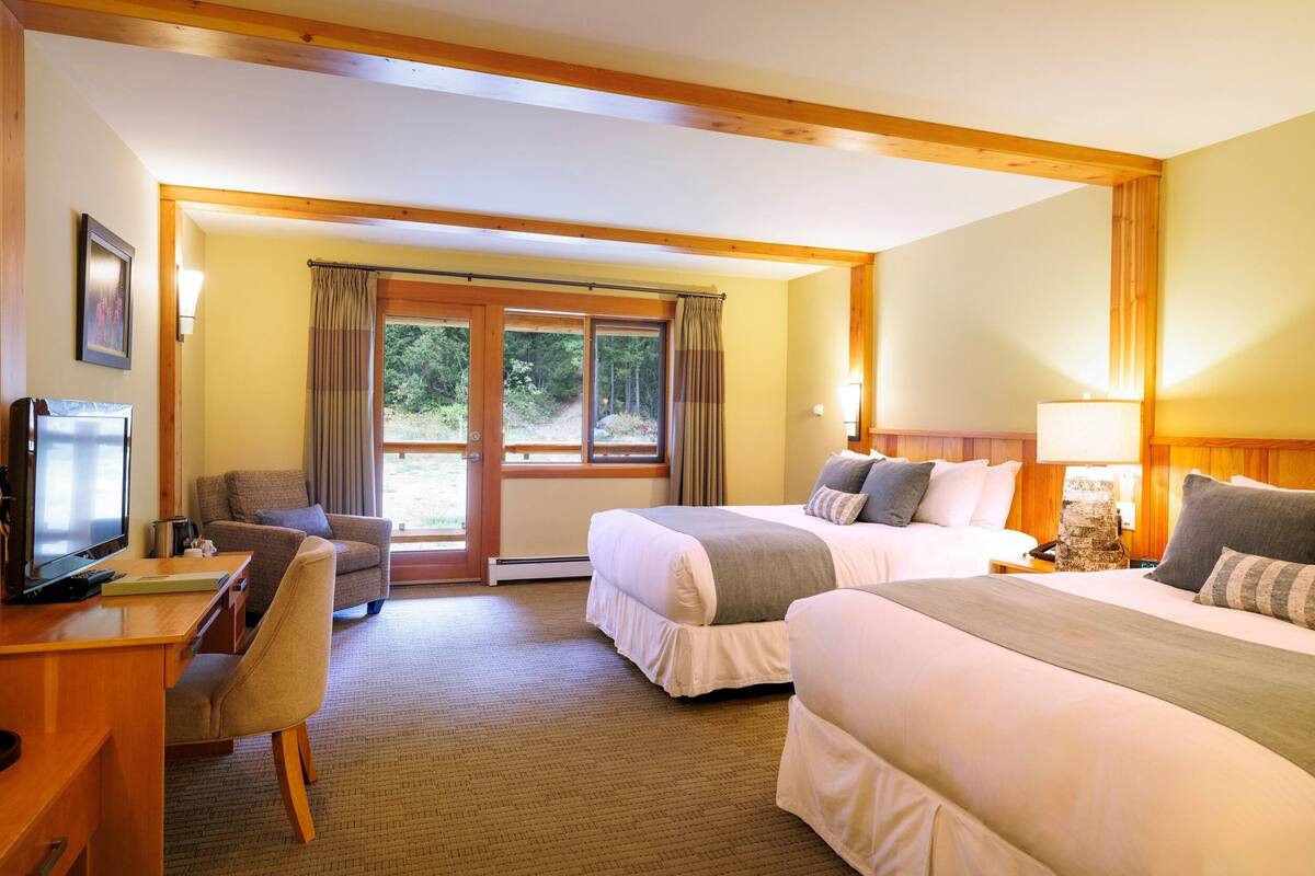 A hotel room with two beds, a desk with a computer, a chair, and a television.